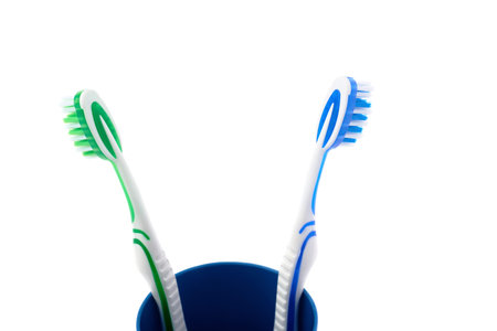 Pair of green and blue toothbrushes in blue plastic cup isolated over white background, quarrel...