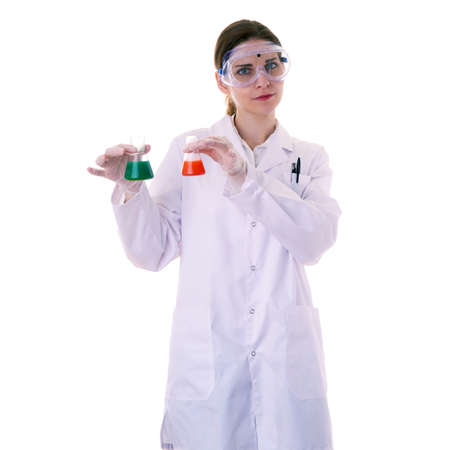 Female assistant scientist in white coat and plastic protective glasses over white isolated background apprehensively holding flasks with substance, healthcare, profession, science and conceptの写真素材