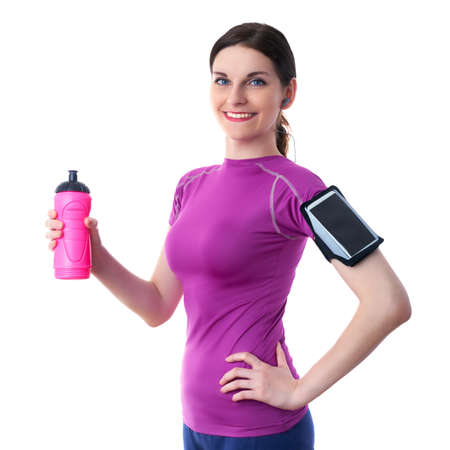 Smiling sporty woman in violet T-short with pink drinking bottle, smart phone device and headphones over white isolated background, fitness, sport and lifestyle conceptの写真素材