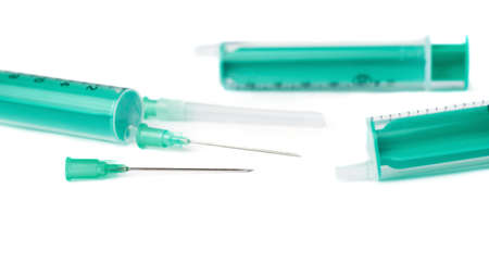 Three one-off green medical syringes with needles lying isolated over white backgroundの写真素材
