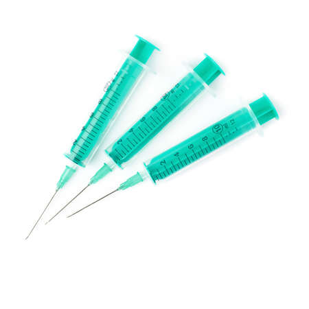 Three one-off green medical syringes with needles lying isolated over white backgroundの写真素材