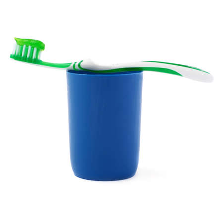 Green single toothbrush with paste lying on blue plastic cup isolated over white backgroundの写真素材
