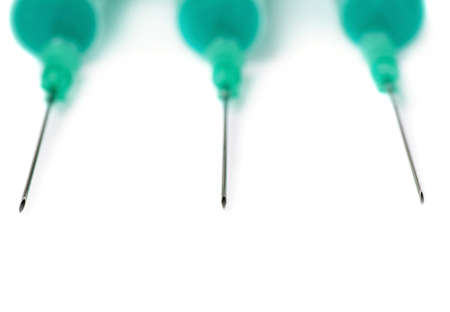 Three one-off green medical syringes with needles lying isolated over white backgroundの写真素材