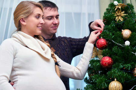 young pregnant woman and happy father decorating christmas tree - pregnancy, holiday, family and expectation conceptの写真素材