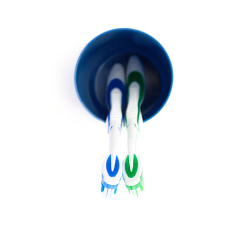 Pair of green and blue toothbrushes in blue plastic cup isolated over white background, love...