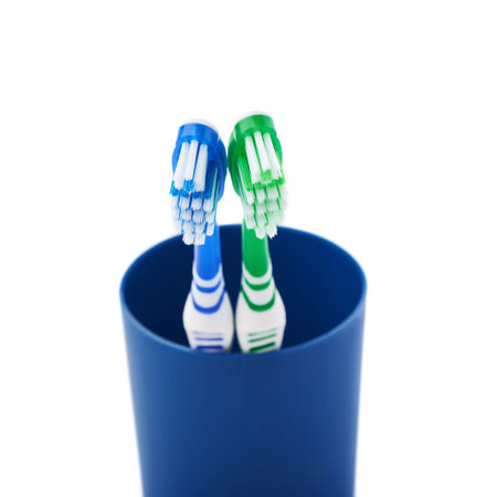 Pair of green and blue toothbrushes in blue plastic cup isolated over white background, love togetherness love conceptの写真素材