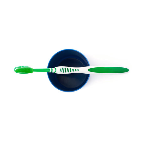Green single toothbrush with paste lying on blue plastic cup isolated over white background