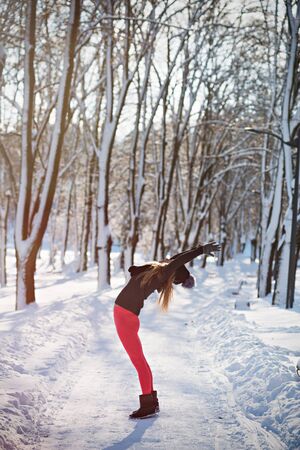 Beautiful woman doing yoga outdoors in the snow at winter timeの写真素材