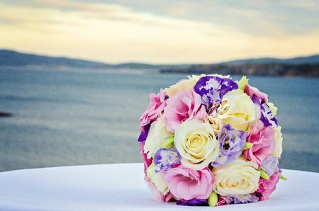 Yellow pink and purple wedding bouquet from roses. Beach and sea backgroundの写真素材