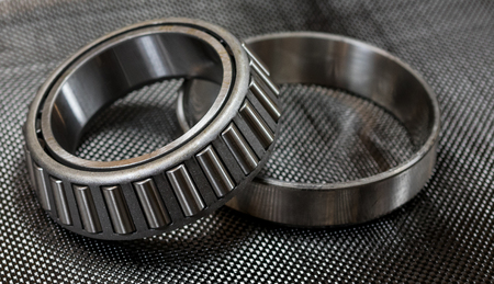 Antique automotive tapered roller bearing and race on plain weave carbon fiber cloth.の写真素材