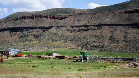 Desert farm in a valley canyon gorge with green grass and a rocky cliff in the distanceの写真素材