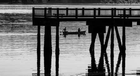 Black and white minimalist scene of a harbor with a canoe under a pier in the water