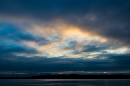Cloudy blue golden yellow sky sunrise sunset over clear waterの写真素材