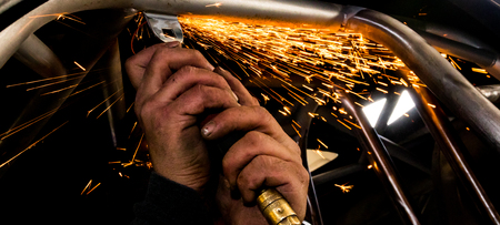 Man grinding steel tubing with a hot pneumatic grinding disc showering sparks and slagの写真素材
