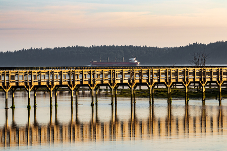 Cargo ship above a wooden board walk on the water with reflectionの写真素材