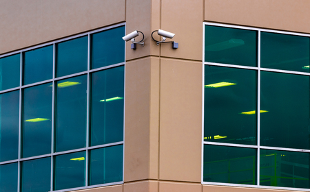 2 security cameras on the side of a building with windows and a sensorの写真素材