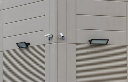 2 security cameras on the side of a building with 2 lightsの写真素材