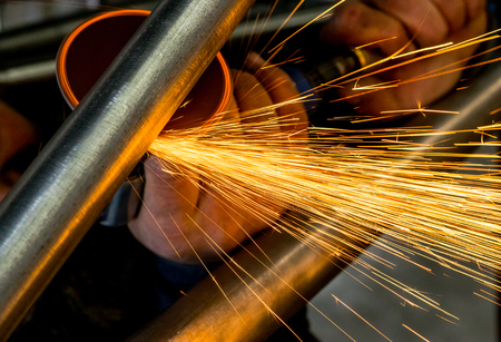 Man grinding steel tubing with pneumatic grinding disc showering sparks and hot slagの写真素材
