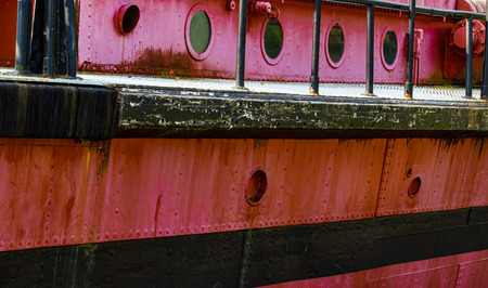 Portholes and deck on an old red rusty boat with a black stripeの写真素材
