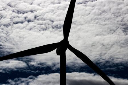 Green sustainable energy windmill power turbine electricity generator on rolling hills with clouds...