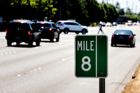 Mile Marker 8 sign on a post with traffic and a road showing treesの写真素材