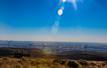 Green sustainable energy windmill power turbine electricity generators on rolling hills with clouds and blue sky aboveの写真素材