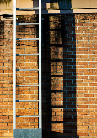 Ladder casting shadow on a worn old stained brick wall in sunlightの写真素材
