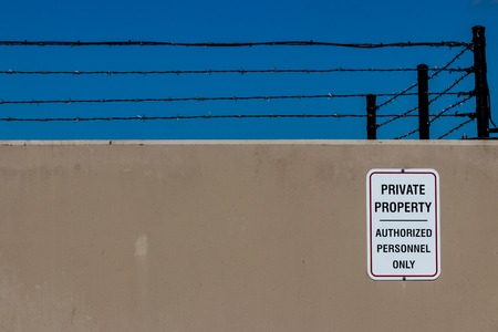 Concrete wall with a private property sign and barbed wire and a blue skyの写真素材