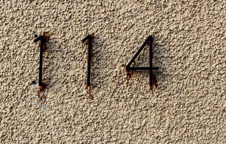 Old grungy white rock wall with the numbers 114 hastily glued with runny adhesiveの写真素材