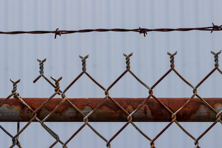 Old rusty chain link barbed wire fence with white wall