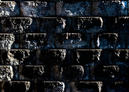 Aged worn grungy cement block wall with dirt and moss showing angled lightの写真素材