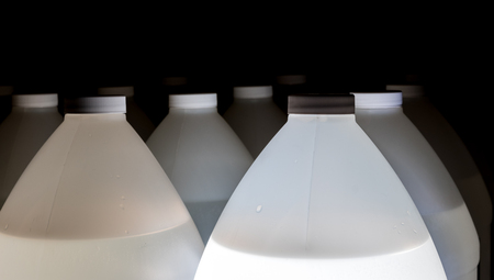 White plastic containers full of fluid with lids and black backgroundの写真素材