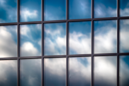 Abstract skyscraper glass window with clouds in reflection and blue skyの写真素材