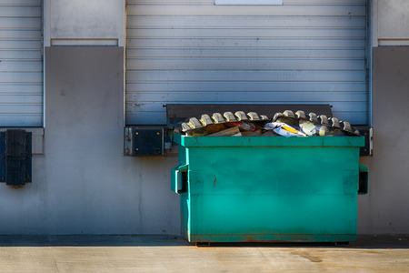Warehouse exterior wall with garage door and garbage bin in daylightの写真素材