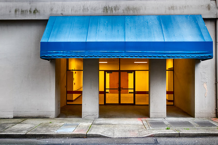 City building entrance with blue awning and yellow light from insideの写真素材