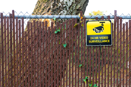 24 hour video surveillance sign on a fence with a treeの写真素材