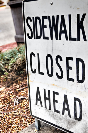 Abstract sidewalk closed ahead sign with plants in the distanceの写真素材