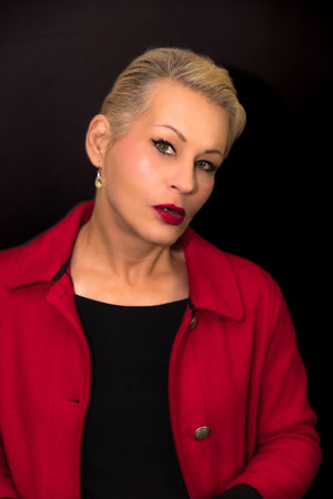 Attractive blonde woman wearing a red coat on a black backgroundの写真素材