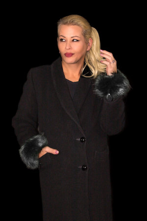 Attractive blonde woman wearing a black cashmere coat on a black backgroundの写真素材