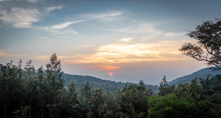 Sun is setting in the deep hill forests with its orange light in blue cloudy sky.の写真素材