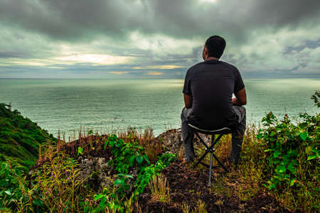 man sitting at mountain cliff enjoying the breathtaking view of sea horizon at morning image is taken at gokarna karnataka india.の写真素材