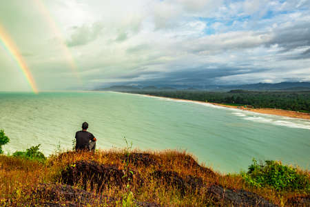 man sitting on hilltop enjoying amazing landscape of sea shore image is taken at gokarna karnataka india. the view from here is pristine and mesmerizing.の写真素材