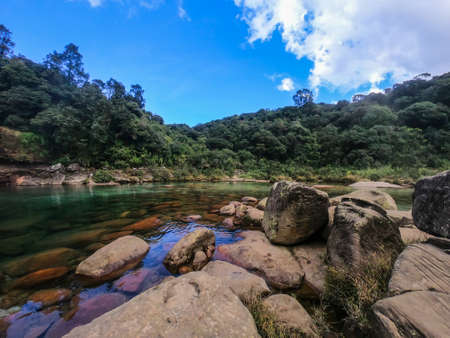 rocks leading to the river clear water surrounded with forests and bright blue sky image taken at lyngksair falls meghalaya.の写真素材