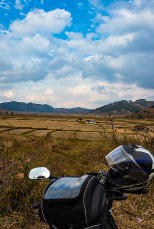 motorcycle view of countryside farming fields surrounded with mountain and blue sky at morning image...