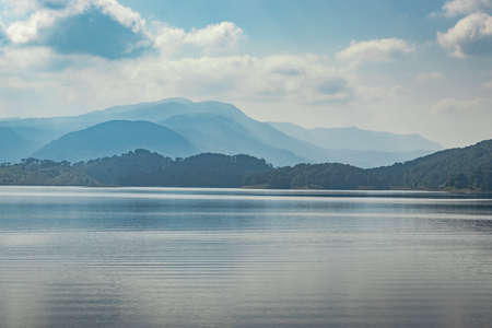 lake serene blue water with misty mountains and clouds reflections image is taken at umiam lake shillong meghalaya india. it is showing the breathtaking beauty of nature.の写真素材