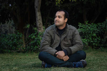 young man different moods of expression cross leg sitting in a park from flat angleの写真素材