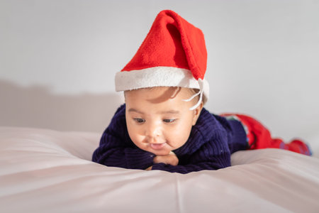 infant boy wearing Christmas red cap lying cute facial expression with white background at indoor