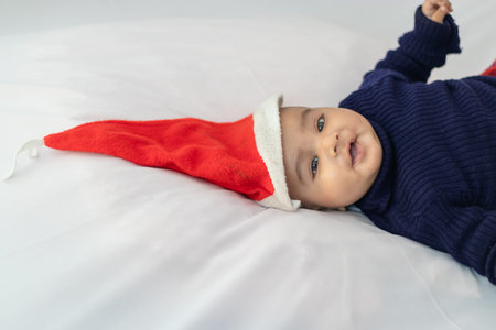 infant boy wearing Christmas red cap lying cute facial expression with white background at indoor