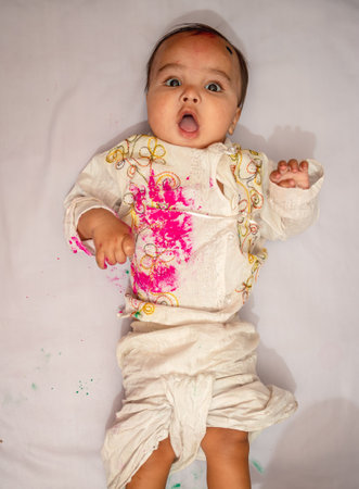 infant lying at bed and paying holi in traditional dress with multicolor from top angleの写真素材