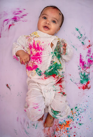 infant lying at bed and paying holi in traditional dress with multicolor from top angleの写真素材